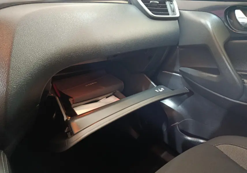Intérieur du Nissan Qashqai 2019 gris clair, vue sur la boîte à gants ouverte côté passager avec documents visibles.