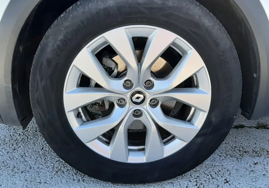 Gros plan sur la roue avant gauche d’un Renault Captur blanc nacré avec jante alliage argentée à 5 doubles branches.