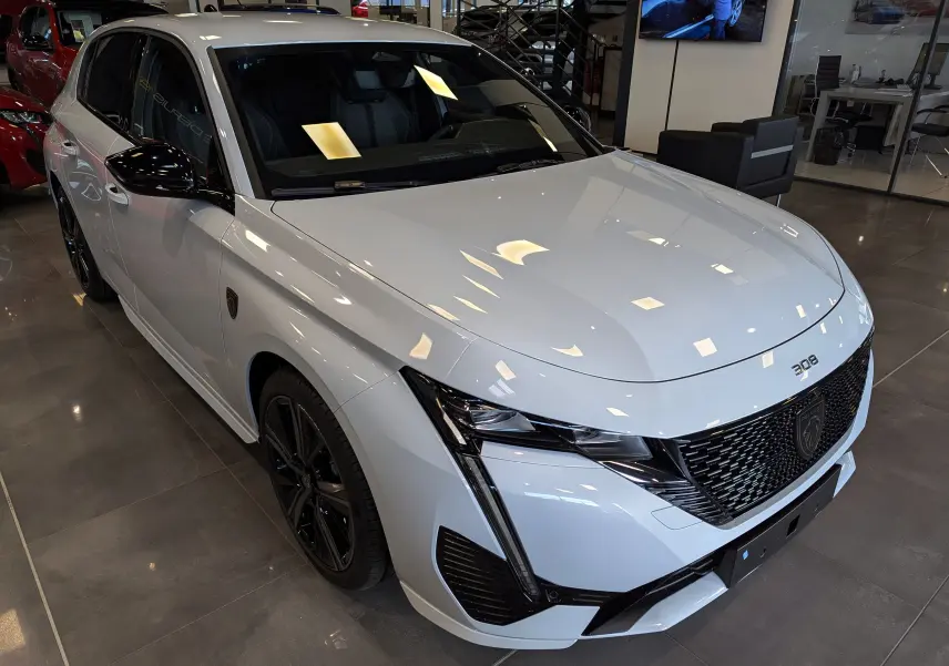 Peugeot 308 GT blanc Okénite vue 3/4 avant droit en showroom, avec calandre noire et jantes noires brillantes.