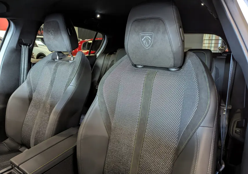 Gros plan sur les sièges avant en cuir noir et tissu avec logo Peugeot brodé sur appuie-tête dans une 308 GT 2025.