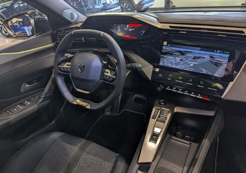 Vue intérieure côté conducteur de la Peugeot 308 GT 2025 avec volant compact GT, écran tactile large et finitions noires élégantes.