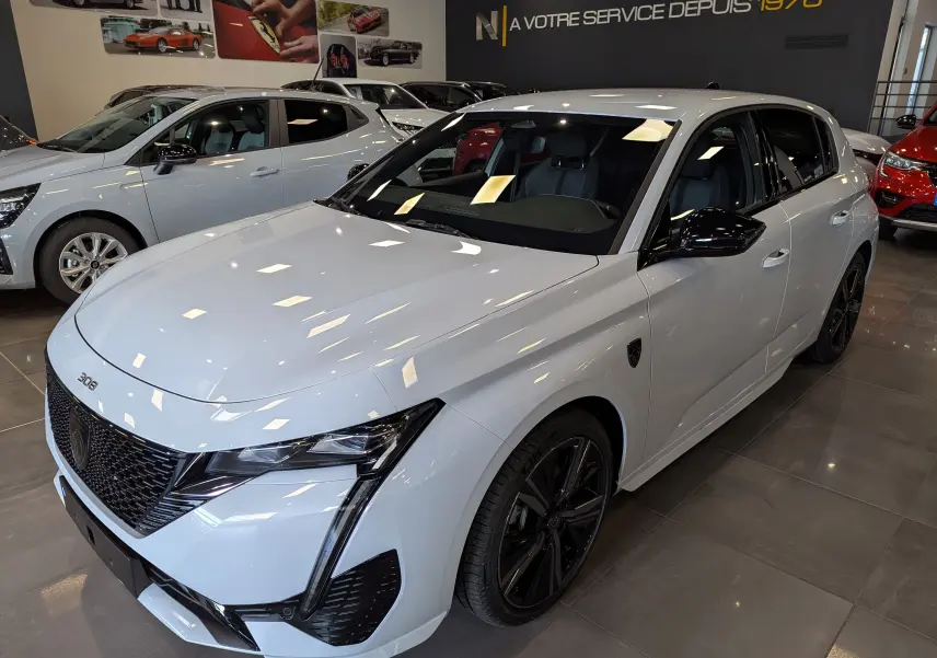 Vue 3/4 avant droite d'une Peugeot 308 GT blanche Okénite avec jantes noires et calandre distinctive en concession.