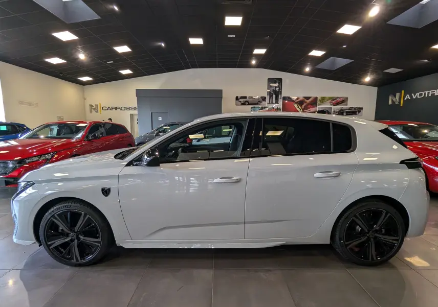 Profil côté gauche d'une Peugeot 308 GT blanche Okénite avec jantes noires dans un showroom lumineux.
