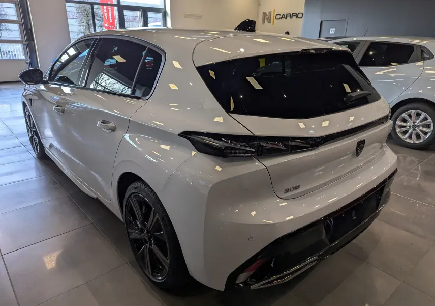 Vue 3/4 arrière gauche d'une Peugeot 308 GT blanche Okénite avec jantes noires en showroom.