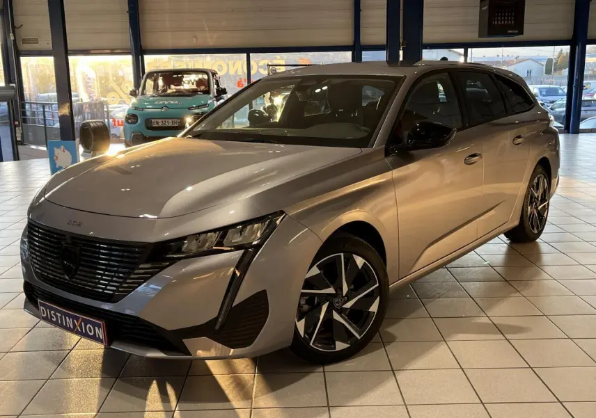 Peugeot 308 SW gris clair métallisé vue 3/4 avant droit en showroom avec jantes alliage distinctives.