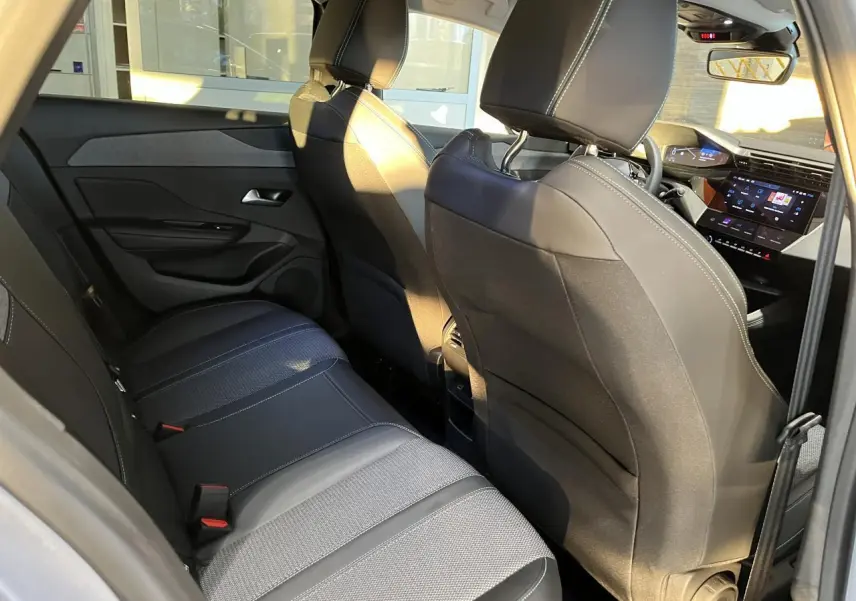 Intérieur arrière du Peugeot 308 SW 2024, vue côté gauche, sièges noirs avec surpiqûres blanches et tableau de bord numérique visible.