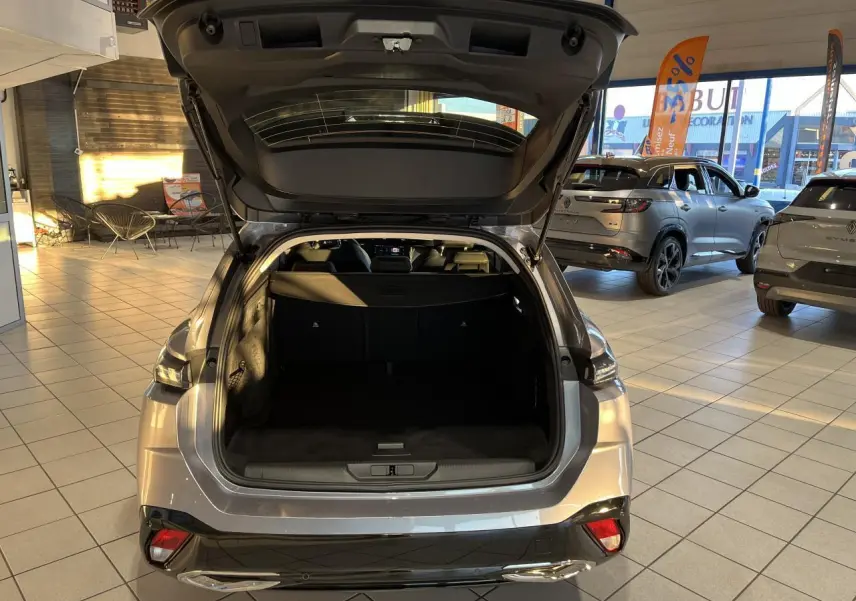 Vue arrière ouverte sur le coffre d'une Peugeot 308 SW 2024 gris clair Metal Artense en concession lumineuse.