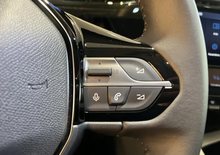 Gros plan sur les commandes du volant côté gauche du Peugeot 308 SW gris clair métal Artense 2024, version diesel.