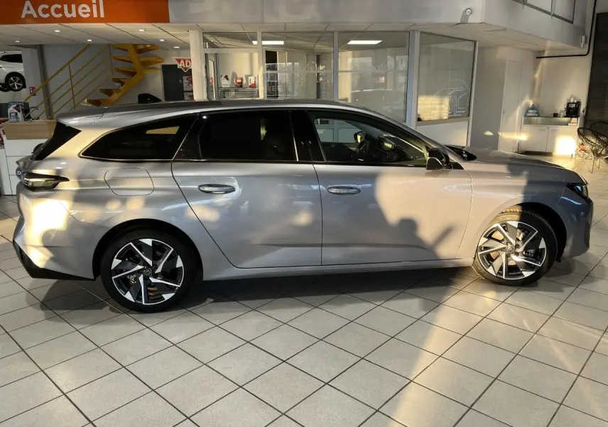 Peugeot 308 SW 2024 gris clair métal Artense vue de profil côté gauche en intérieur avec jantes alliage distinctives.
