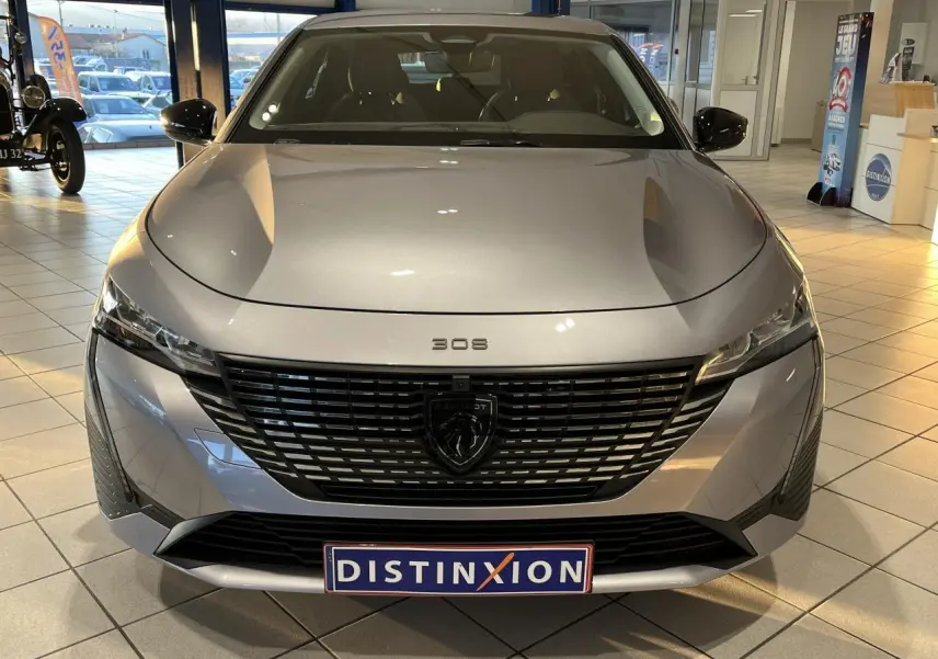 Vue frontale d'une Peugeot 308 SW gris clair Metal Artense 2024 avec calandre noire et logo lion central.