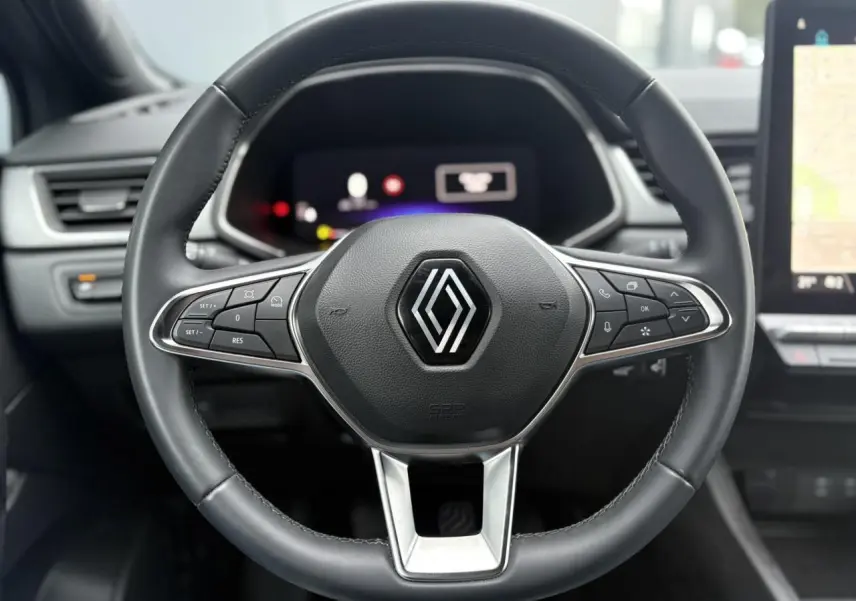 Vue rapprochée du volant noir du Renault Captur 2025 avec commandes intégrées et tableau de bord numérique en arrière-plan.