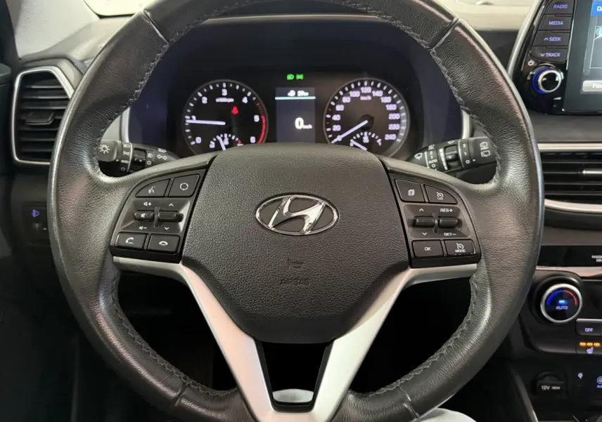 Vue rapprochée du volant en cuir noir du Hyundai Tucson 2019, avec commandes multifonctions et tableau de bord lumineux.