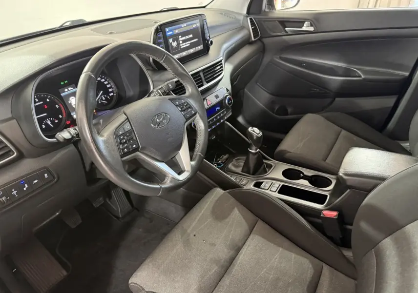 Vue intérieure côté conducteur du Hyundai Tucson 1.6 CRDI noir, volant cuir multifonctions et écran tactile 8 pouces visible.