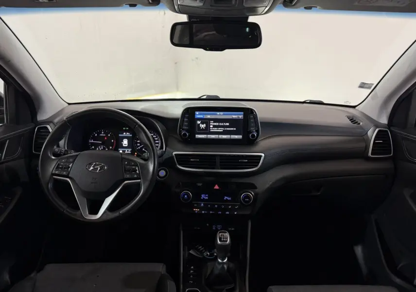 Vue intérieure avant du tableau de bord noir du Hyundai Tucson 1.6 CRDI avec écran tactile et volant multifonctions.