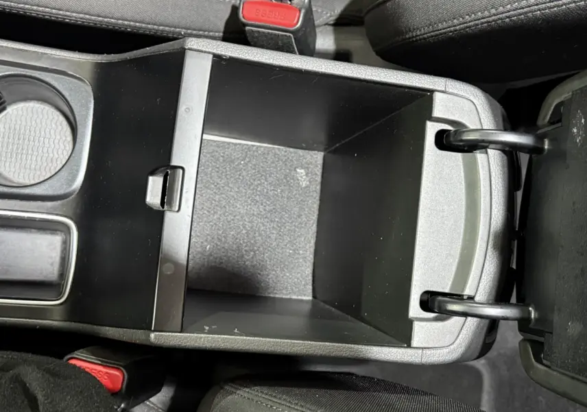 Vue plongeante sur le rangement central ouvert du Hyundai Tucson noir, montrant l'espace intérieur vide et les sièges en tissu noir.