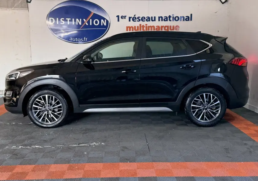 Vue latérale gauche d'un Hyundai Tucson noir 2019 avec jantes alliage et barres de toit noires en intérieur showroom.