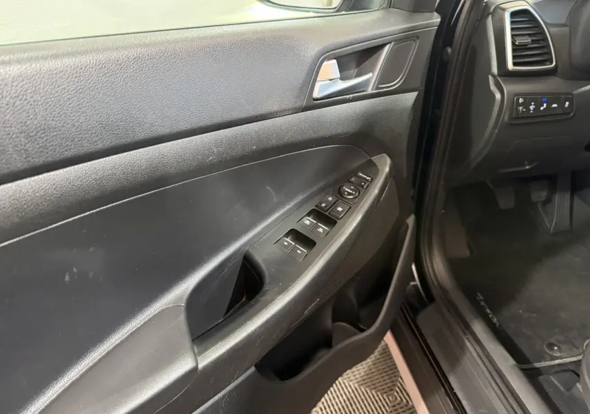 Vue intérieure côté conducteur de la porte noire du Hyundai Tucson 2019 avec commandes électriques des vitres et rétroviseurs.