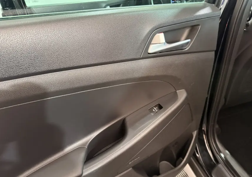 Vue rapprochée de la porte intérieure côté conducteur noire du Hyundai Tucson 2019, avec poignée argentée et commande de vitre.