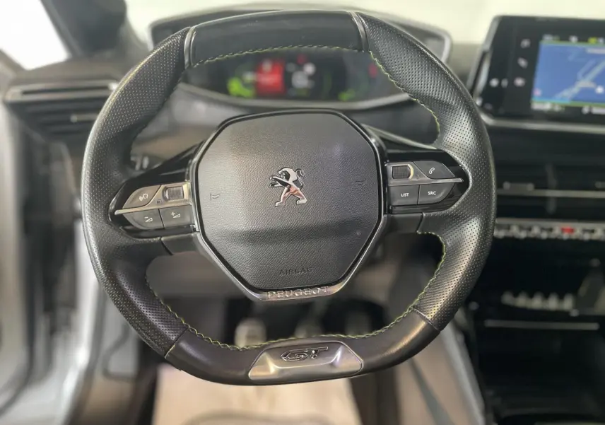 Volant compact cuir noir avec surpiqûres vertes et badge GT au centre du Peugeot 208 gris clair Metal Artense 2023.