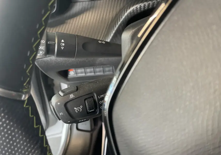 Gros plan sur la commande de régulateur de vitesse à gauche du volant cuir noir sur Peugeot 208 gris clair métallisé.