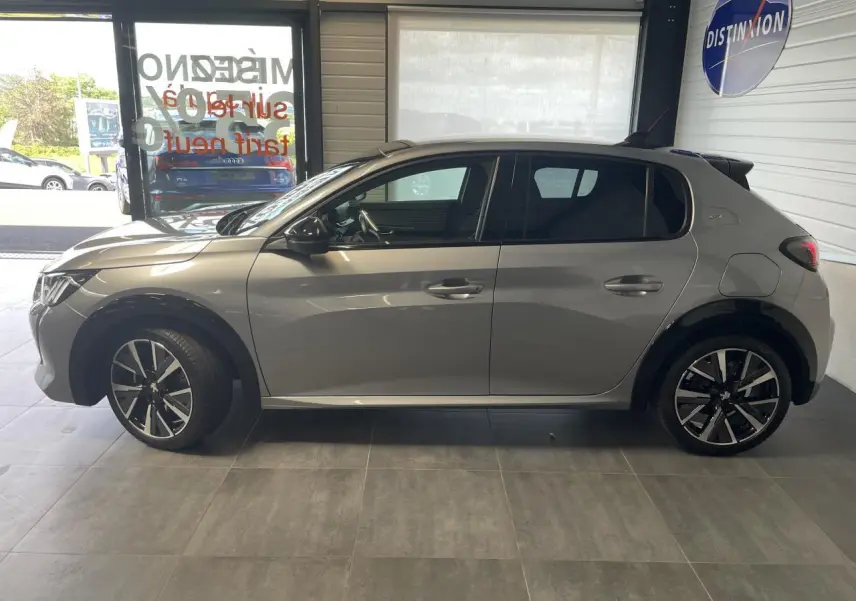 Profil côté gauche d'une Peugeot 208 gris clair métallisé avec toit noir et jantes alliage 17 pouces en showroom.