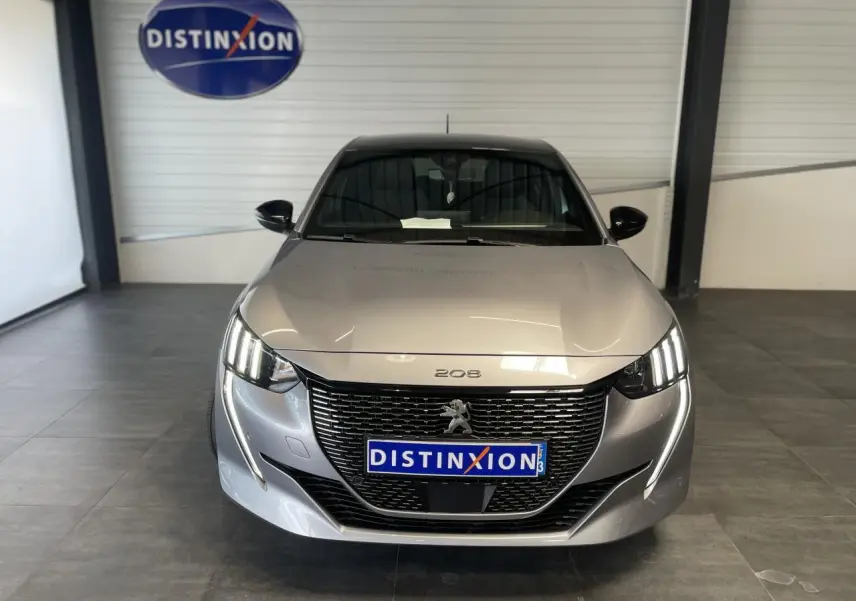 Peugeot 208 gris clair métallisé vue de face en intérieur, avec calandre noire et toit noir brillant.