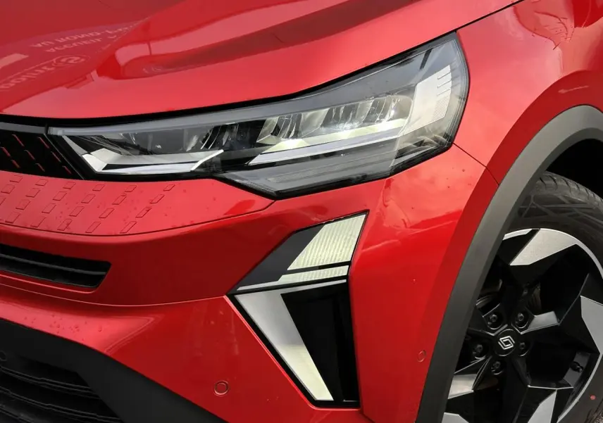 Gros plan sur l’avant droit du Renault Captur 2025 Rouge Flamme/Noir, mettant en valeur le phare LED et la jante alu noire diamantée.