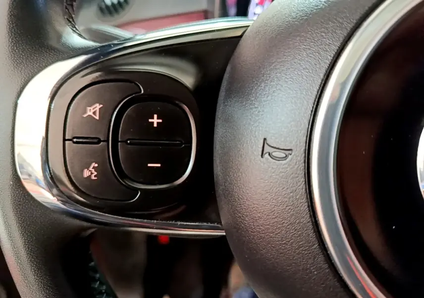 Gros plan sur les commandes gauche du volant noir de la FIAT 500 rouge, avec boutons de volume et reconnaissance vocale.