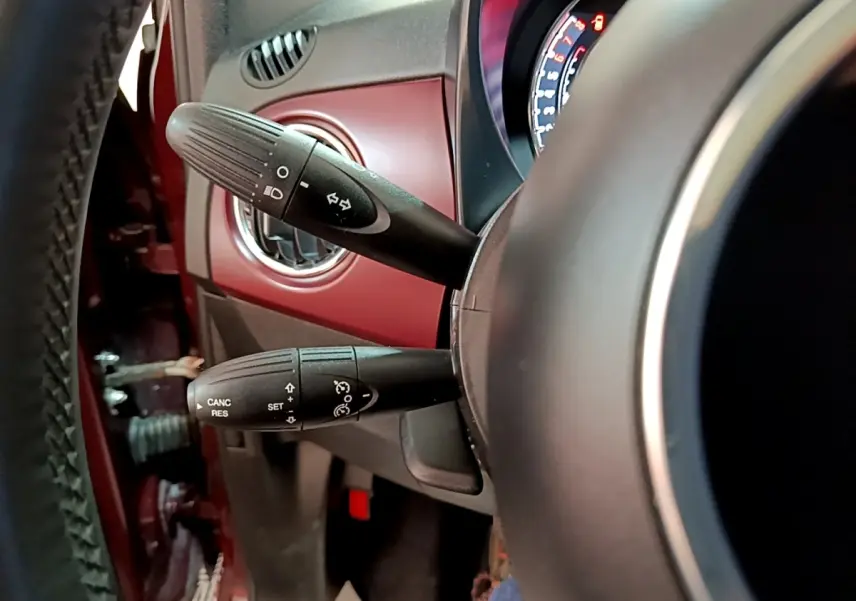 Gros plan sur la colonne de direction d’une FIAT 500 rouge, avec commandes de clignotants et régulateur de vitesse visibles.