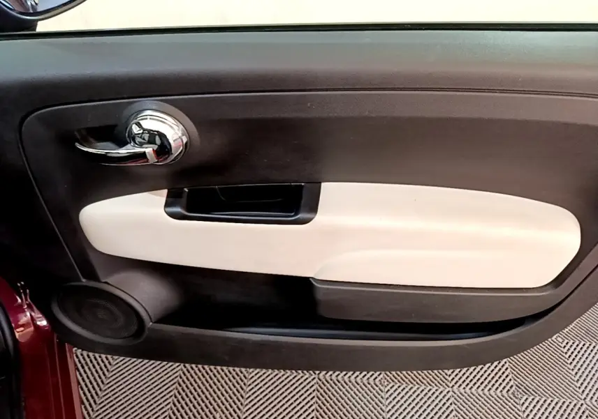 Gros plan sur la porte intérieure côté gauche de la FIAT 500 rouge, avec poignée chromée et insert beige.