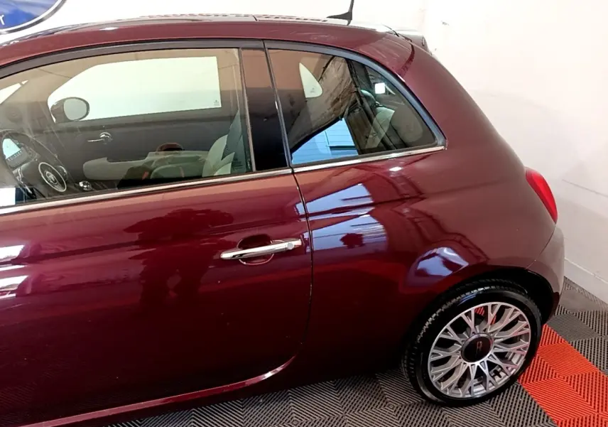 Vue côté droit arrière d'une FIAT 500 rouge bordeaux avec jantes alliage et poignée de porte chromée.