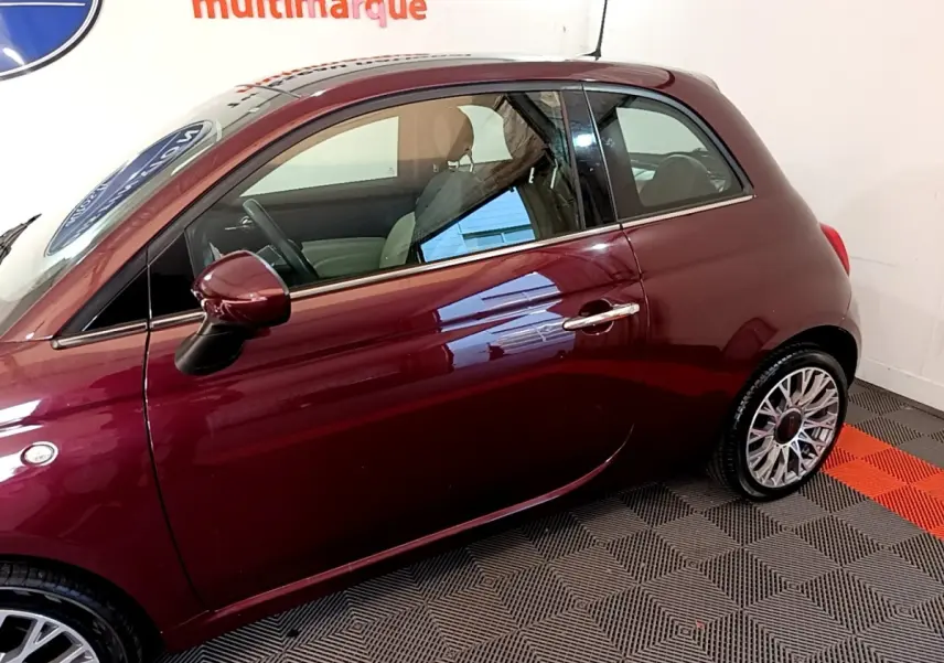 Vue latérale gauche d'une FIAT 500 rouge bordeaux, mettant en valeur la porte et la jante alliage au design complexe.