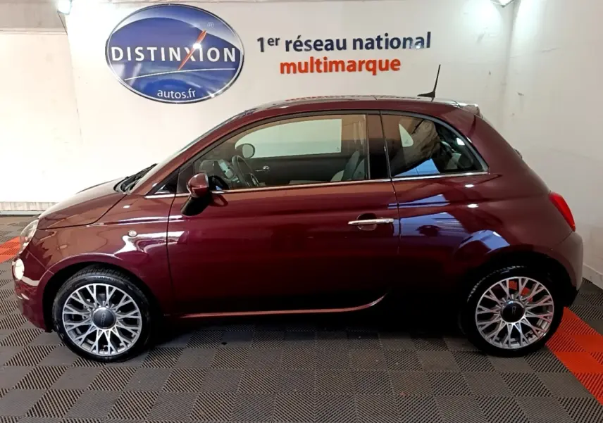Vue de profil côté gauche d'une FIAT 500 rouge bordeaux 2021 avec jantes alliage et toit noir en intérieur showroom.