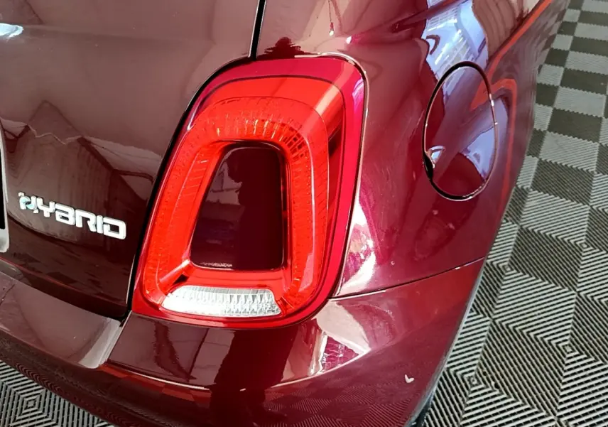 Gros plan sur le feu arrière droit rouge et l’inscription Hybrid d’une FIAT 500 rouge, avec la trappe à carburant visible.