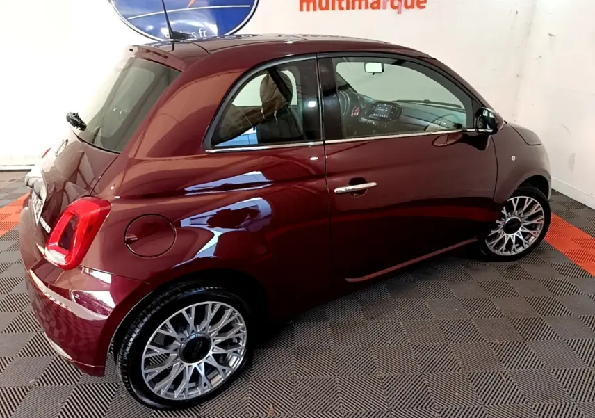 Vue 3/4 arrière droite d'une FIAT 500 rouge brillante avec jantes alliage et intérieur visible.