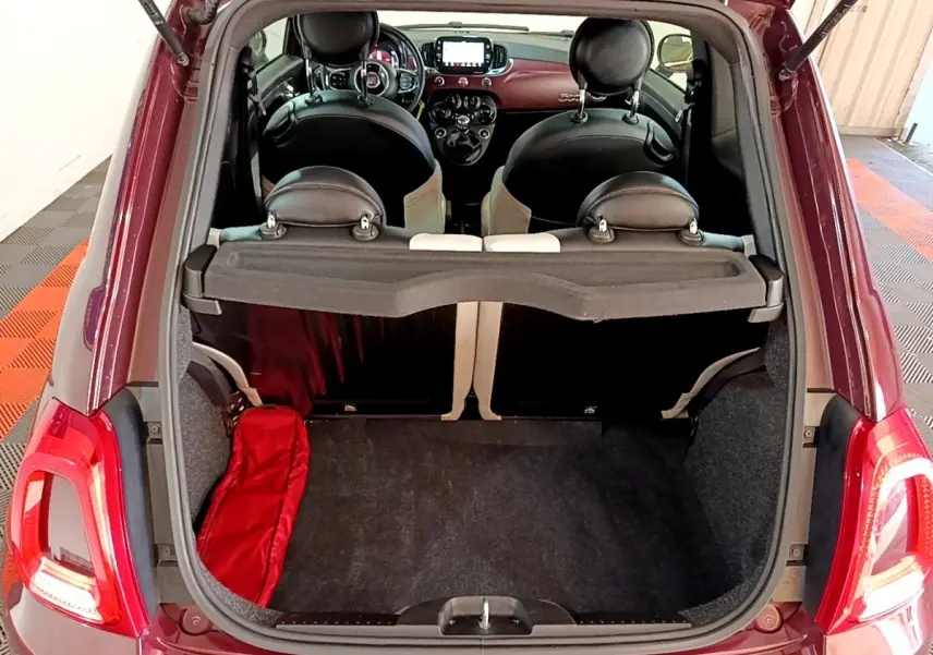 Vue arrière du coffre ouvert d'une FIAT 500 rouge, montrant l'intérieur noir des sièges et le tableau de bord.