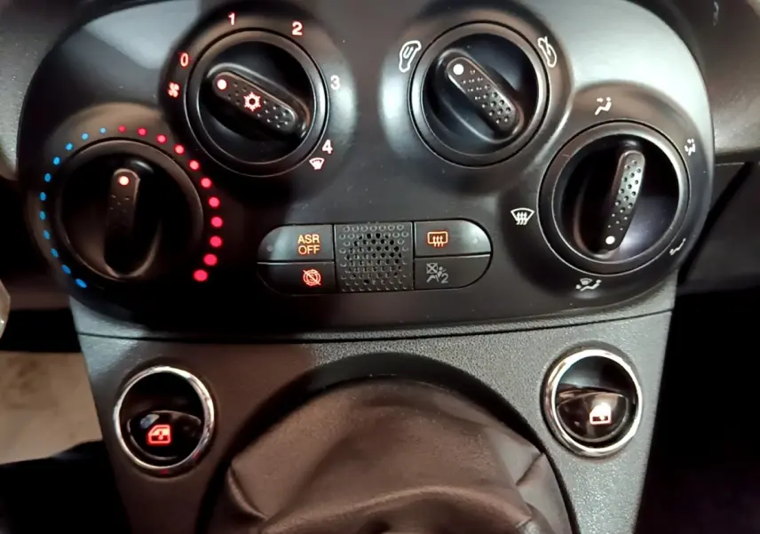 Gros plan sur les commandes de climatisation et vitres électriques d’une Fiat 500 gris foncé, tableau de bord noir.