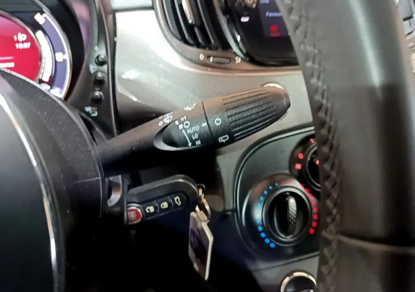 Détail du volant cuir et commandes de climatisation d'une Fiat 500 hybride gris foncé, vue côté gauche.