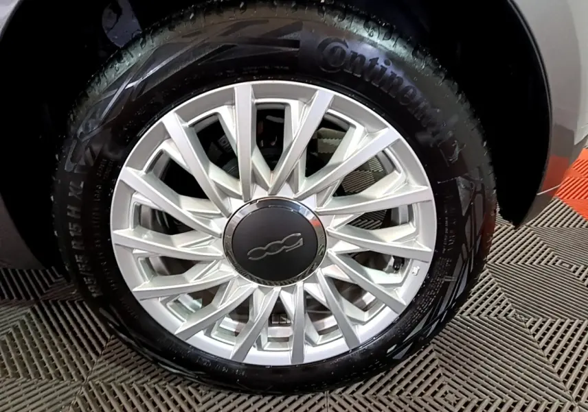 Gros plan sur la roue avant droite d'une FIAT 500 gris foncé, avec jante alliage argentée et logo central 500.