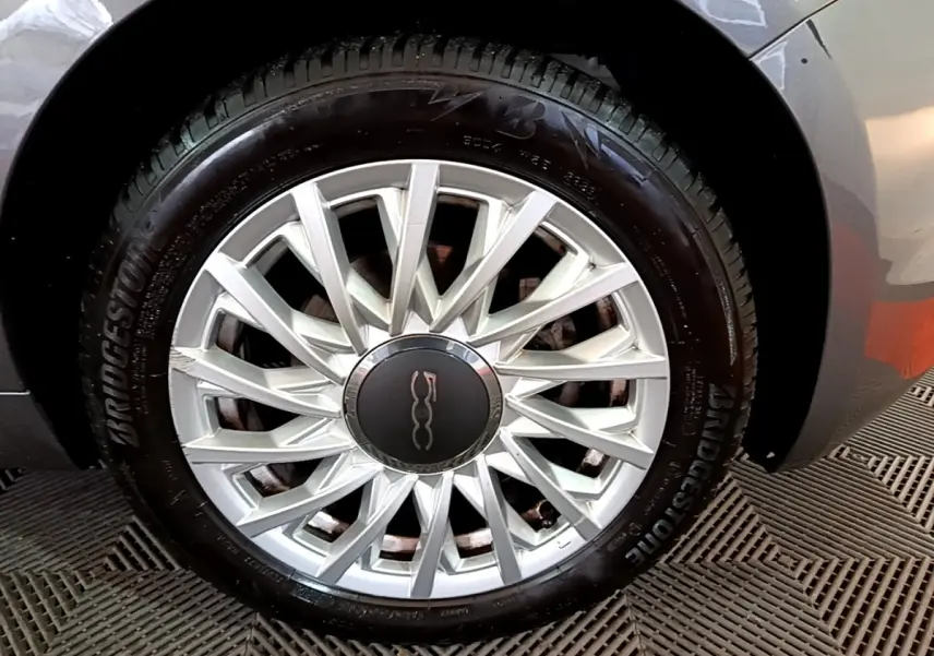 Gros plan sur la roue avant droite d'une FIAT 500 gris foncé avec jante alliage multibranches et logo central.