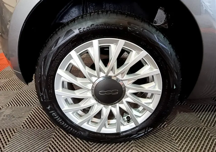 Gros plan sur la roue avant droite d'une FIAT 500 gris foncé, avec jante alliage au design étoilé.