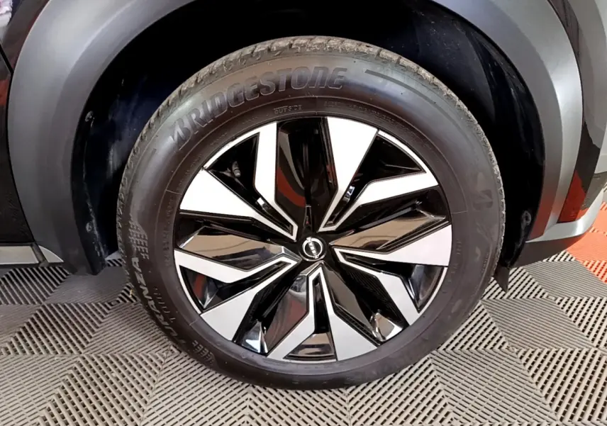 Gros plan sur la roue avant droite du Nissan Juke noir 2023, mettant en valeur la jante bicolore brillante et le pneu Bridgestone.