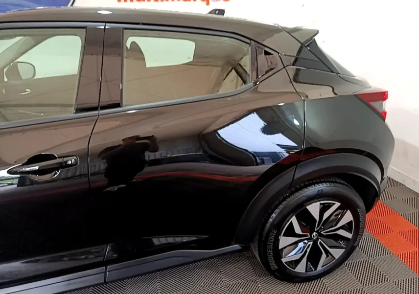 Vue latérale droite du Nissan Juke noir 2023, mettant en valeur la porte arrière et la roue avec jante design bicolore.