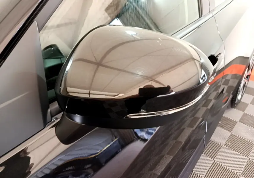 Gros plan sur le rétroviseur droit noir brillant du Nissan Juke 2023, avec reflet du plafond et carrosserie noire visible.