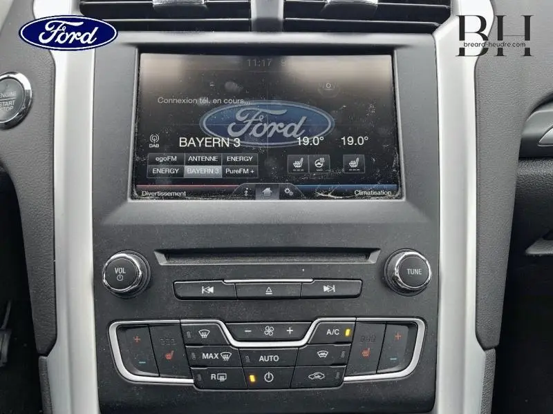 Vue rapprochée du tableau de bord de la Ford Mondeo SW gris Magnetic, avec écran tactile et commandes de climatisation visibles.