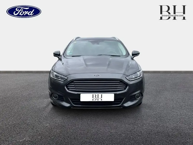 Vue frontale d'une Ford Mondeo SW 2.0 TDCi 150ch Trend gris Magnetic avec calandre chromée et phares allumés.