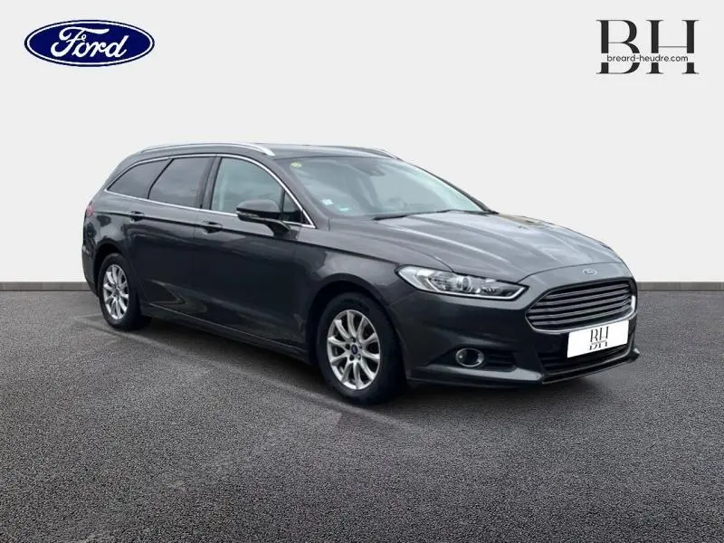 Ford Mondeo SW gris Magnetic vue 3/4 avant droit, avec calandre chromée et barres de toit visibles.