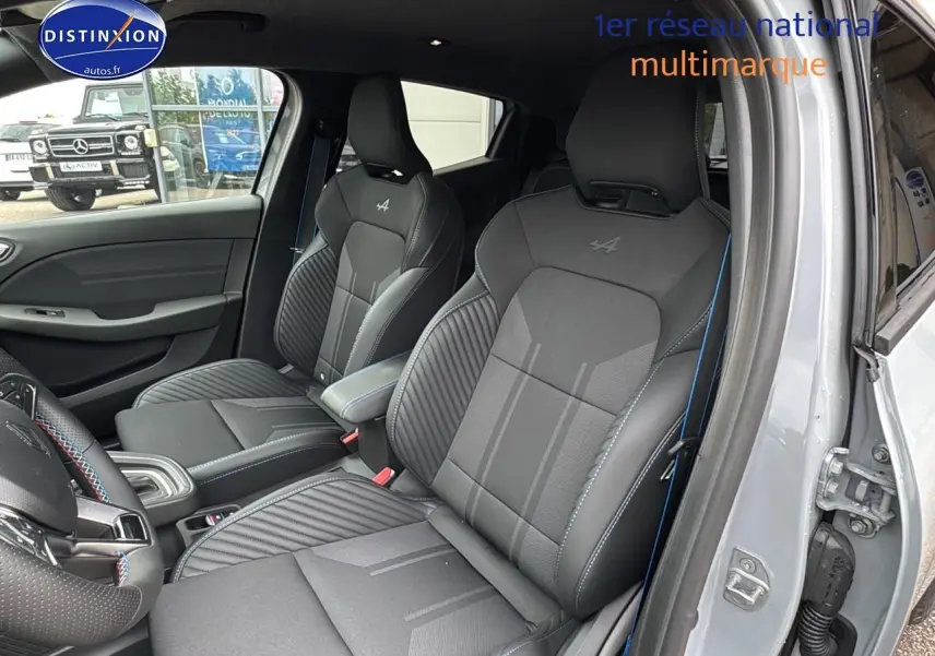 Vue intérieure côté droit de la Renault Clio V gris rafale, sièges sport esprit Alpine avec surpiqûres bleues et accoudoir central.