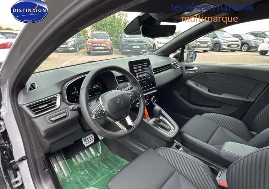 Intérieur avant de la Renault Clio V gris rafale, volant multifonction et écran tactile central visible depuis la porte ouverte côté conducteur.