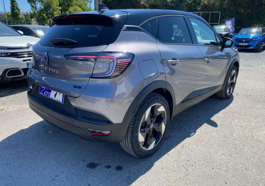Vue 3/4 arrière droite du Renault Captur 1.6 E-Tech Hybride gris Cassiopée avec toit noir étoilé et jantes distinctives.